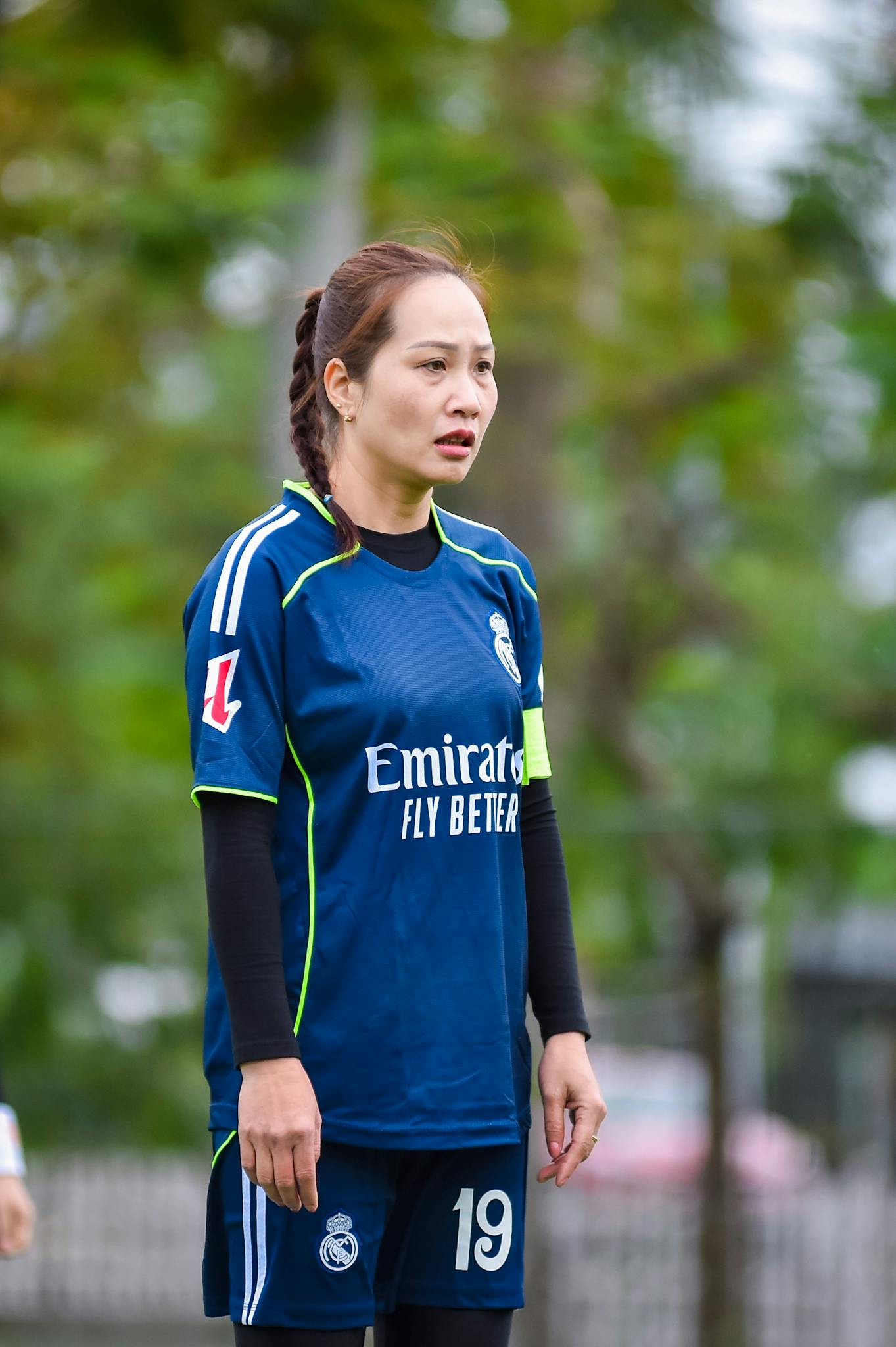 A female football player in a blue jersey on the field in Hà Nội, Vietnam, showing focus and determination.