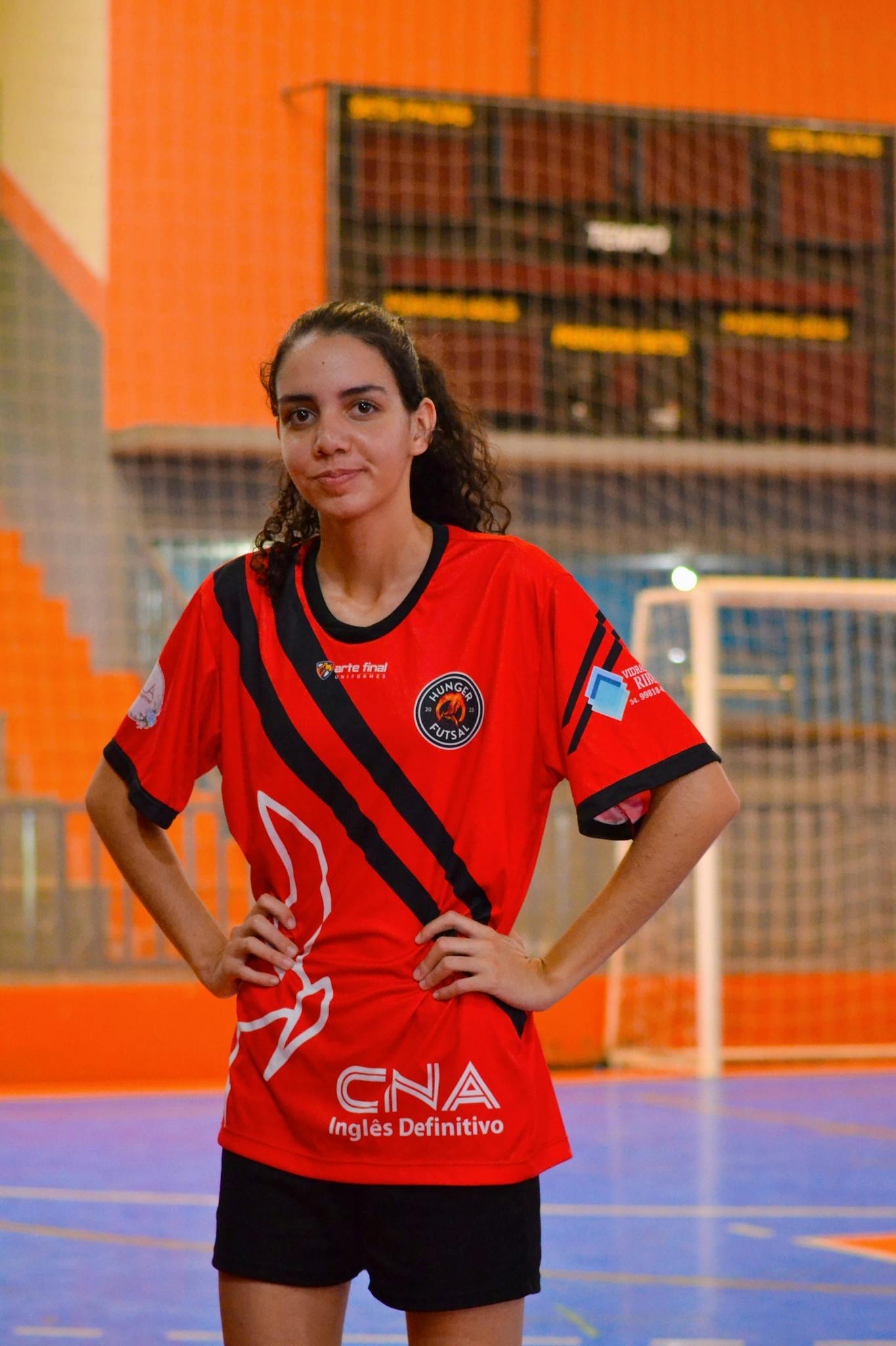 Young female soccer player in a red jersey posed confidently indoors.