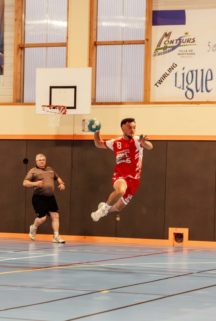 Action shot of a handball player jumping in an indoor sports arena in France.