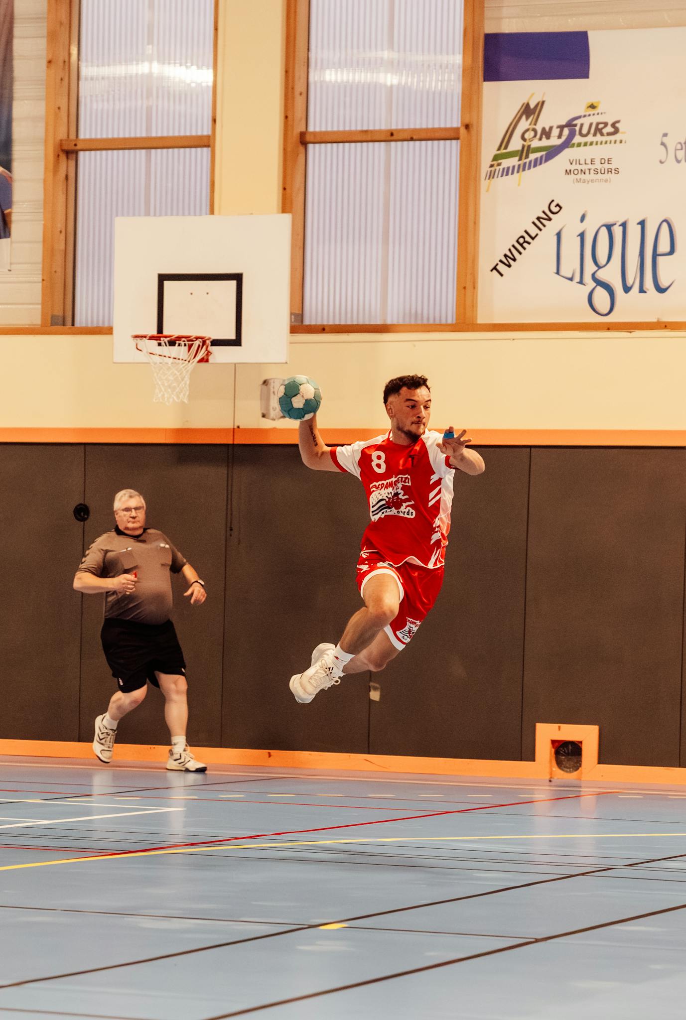 Action shot of a handball player jumping in an indoor sports arena in France.