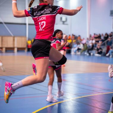 Female handball player jumping in mid-air during an intense match indoors.