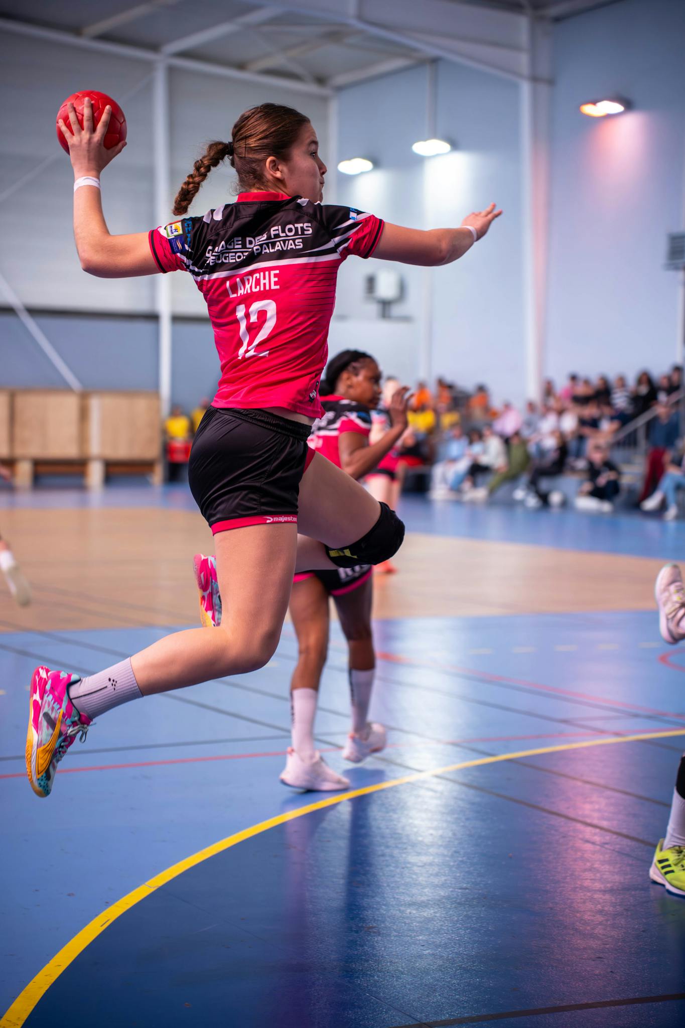 Female handball player jumping in mid-air during an intense match indoors.