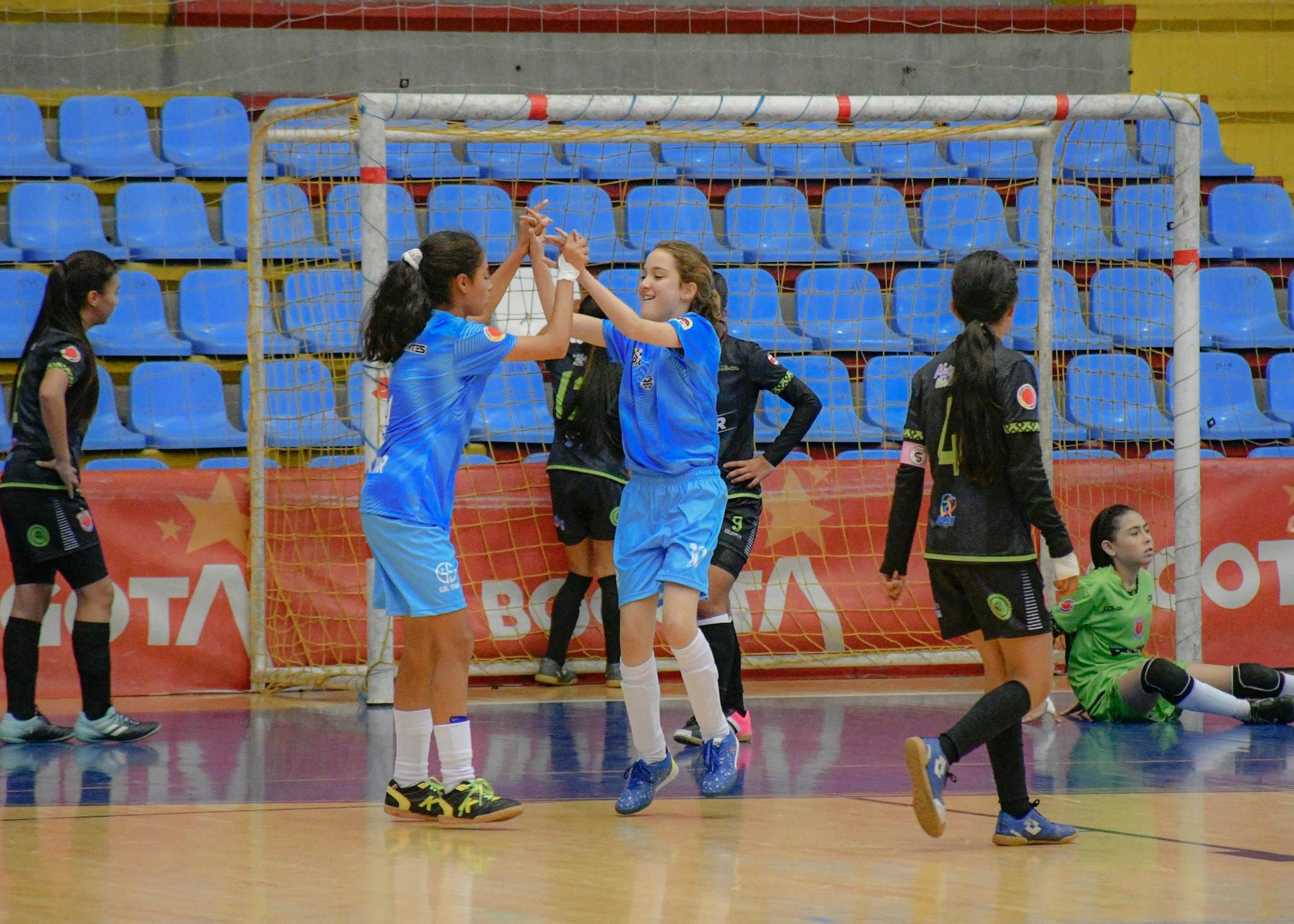 Joyful moment as girls celebrate a goal during an indoor soccer game. Team spirit and excitement fill the gymnasium.